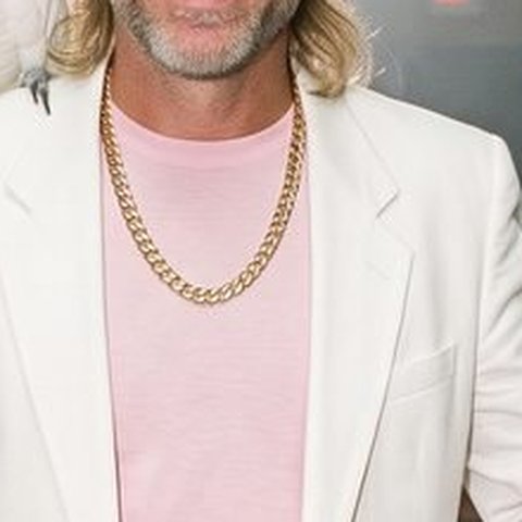 A thick gold Cuban link chain over a pink T-shirt and white suit